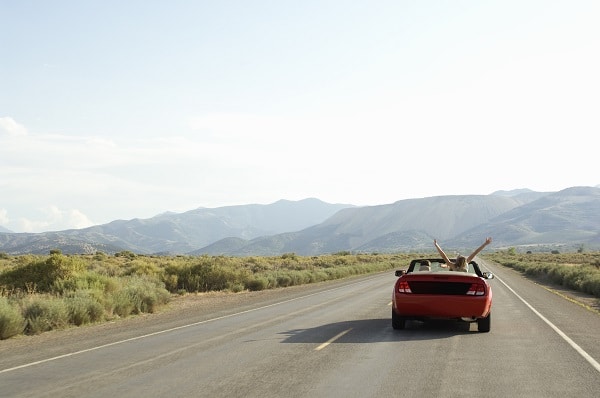 a carefree couple drives down a desert road in a red convertible