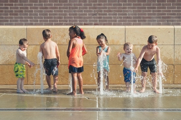 to save money on air conditioning, a group of children play in a public fountain on a summer day